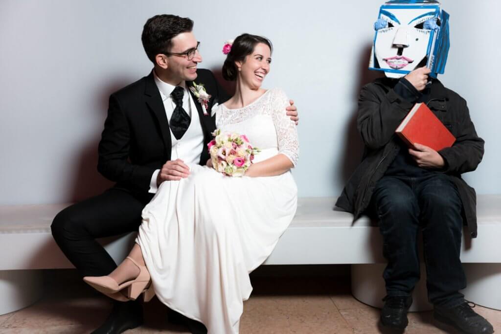 Brautpaar sitzt in der Schirn in Frankfurt auf einer Bank und neben ihnen ein Mann mit einer Maske.