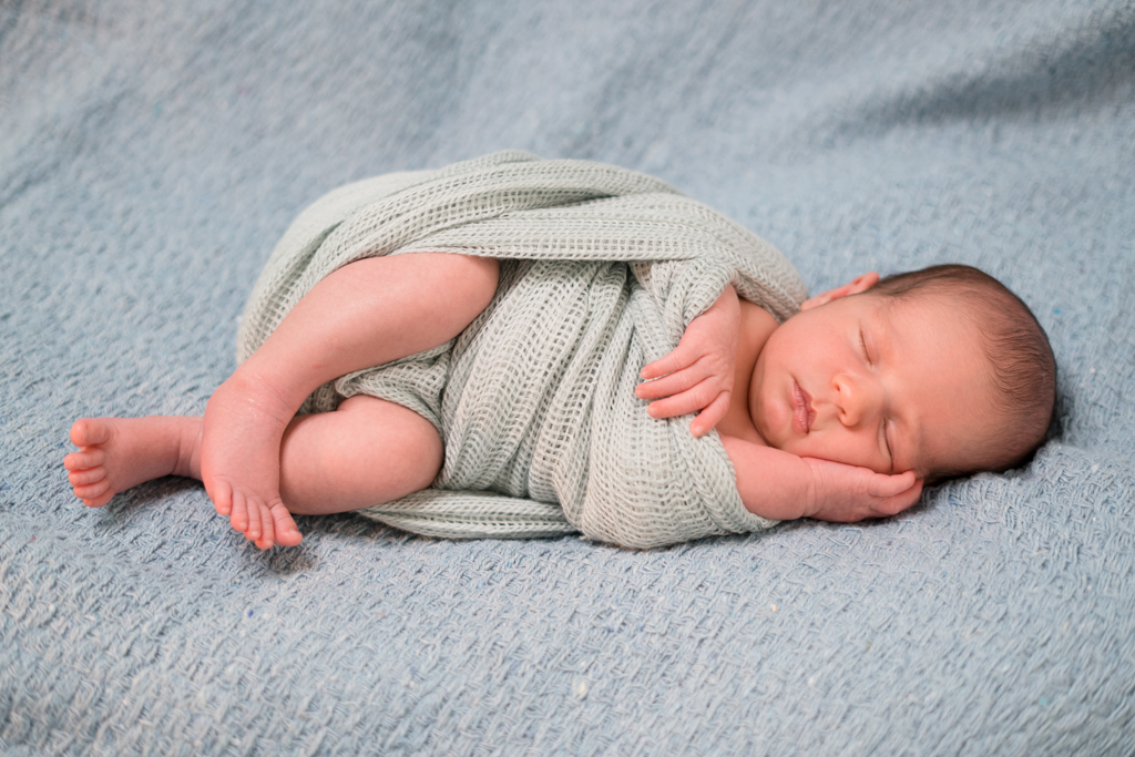 Baby posing auf einer blauen Decke beim Neugeborenen Shooting.