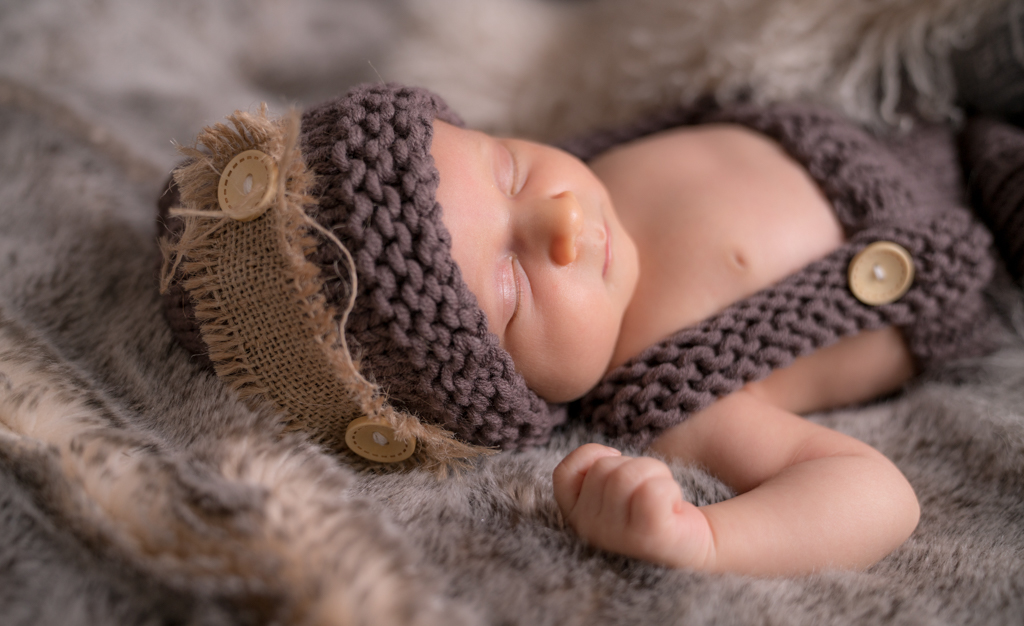 Neugeborenes bei Babyshooting mit Mütze und Fell.