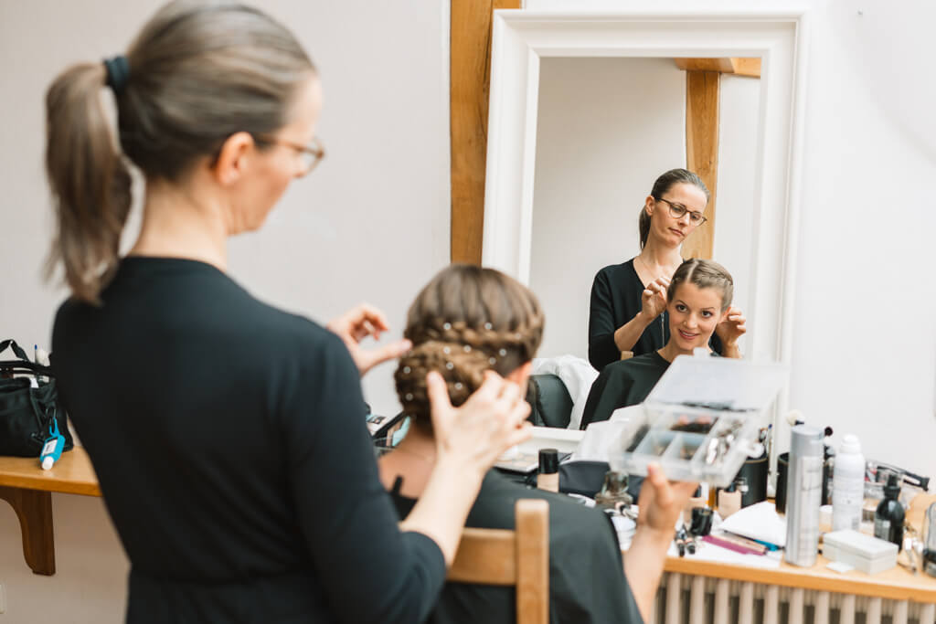 Braut beim Haarstyling schaut in den Spiegel.