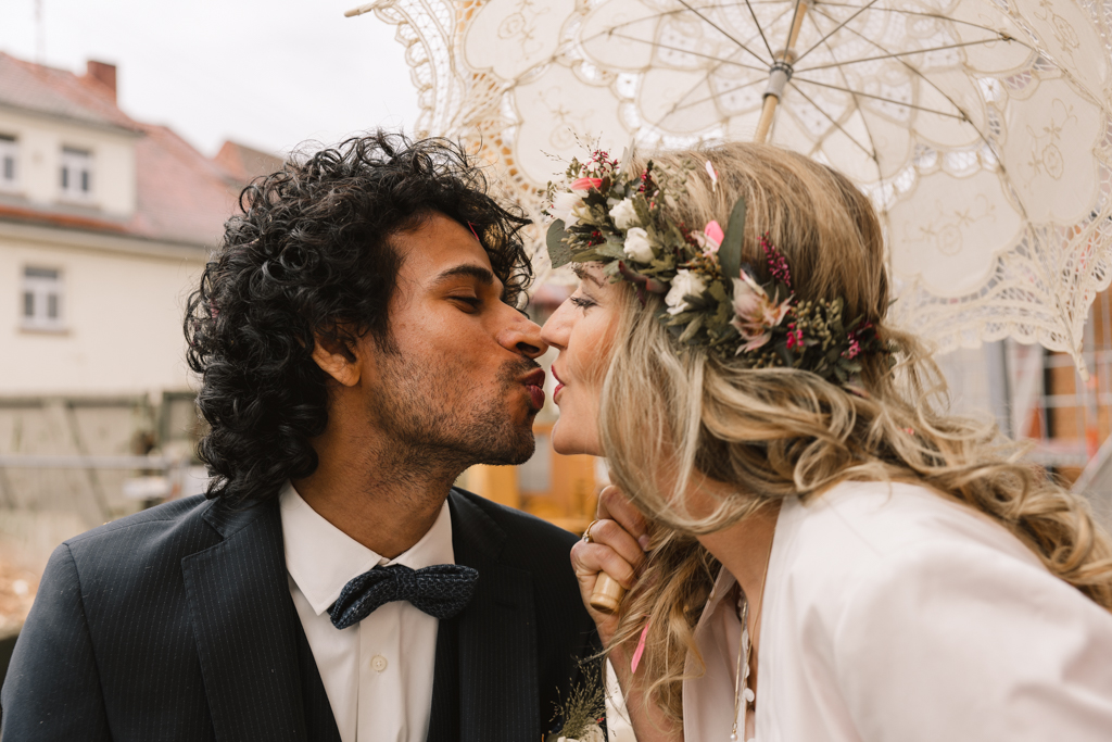 Hochzeitspaar küsst sich mit einem vintage weißen Regenschirm.