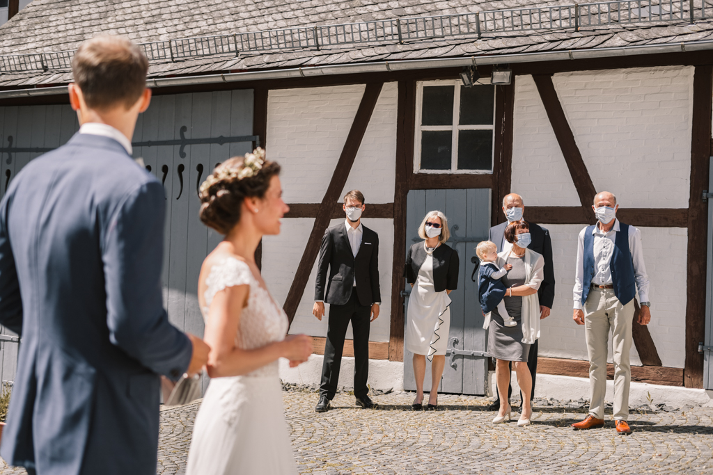 Hochzeitsgesellschaft mit Maske steht an einer Scheune.