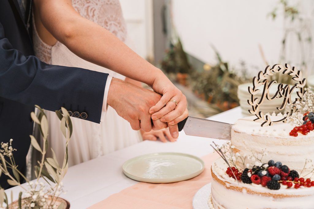 Hände vom Brautpaar beim Hochzeitstorten Anschnitt.