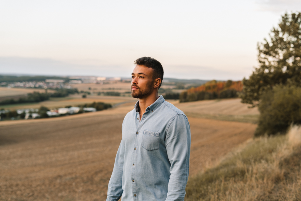 Mann steht auf einem Feld und schaut in die untergehende Sonne.