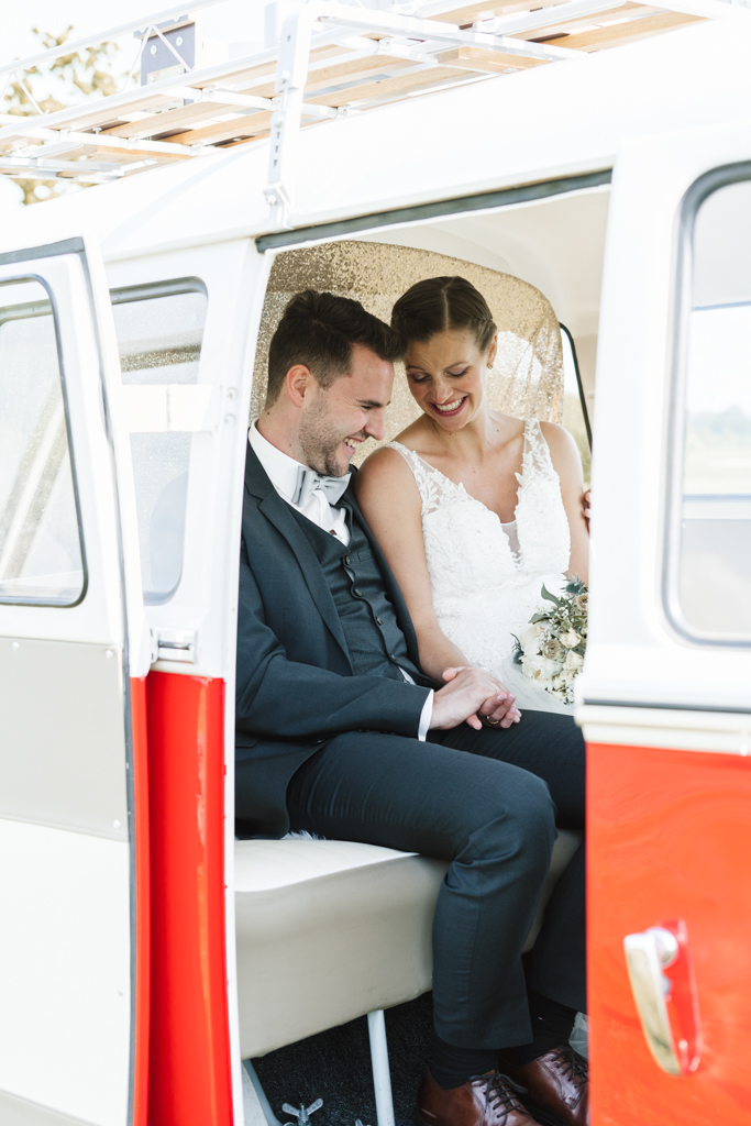 Brautpaar in weiß-rotem Retro Bus und schaut sich die neuen Eheringe an.