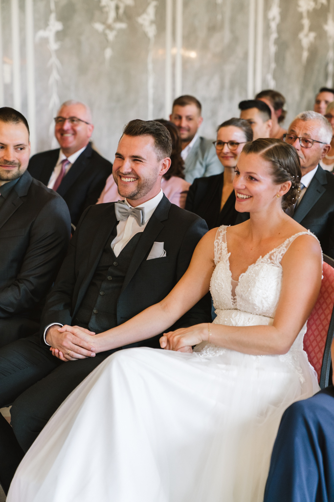 Brautpaar hält während der Hochzeit die Hände und lacht.