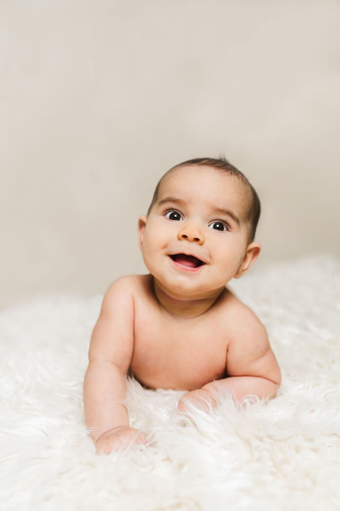 Baby liegt auf einem weißen Lammfell beim Babyshooting und lacht.