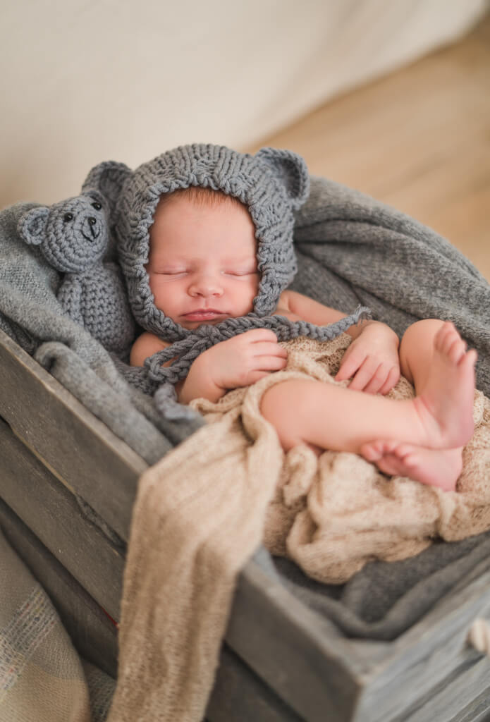 Neugeborenes liegt mit einer Teddy Mütze in einer grauen Kiste während des Neugeborenen Shootings.