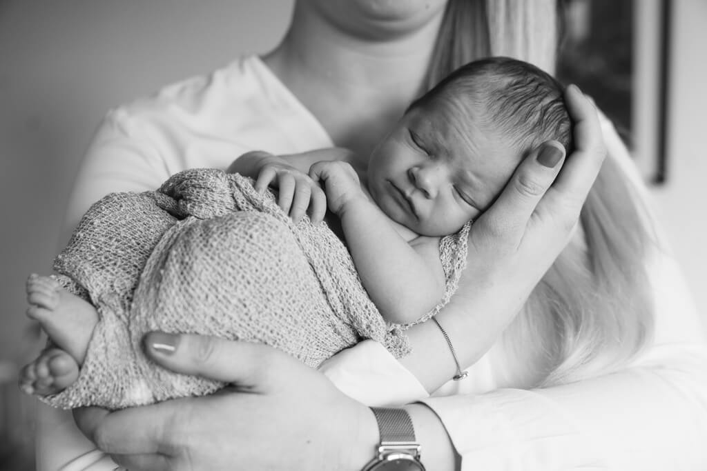 Mutter hält ihr Baby während des Neugeborenen Shooting in den Armen.