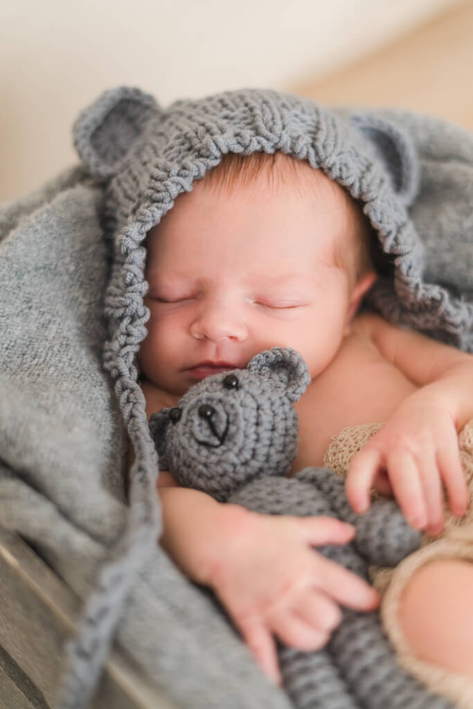 Babyfotografie Frankfurt mit Bärchen Mütze und Kuscheltier in der Hand.