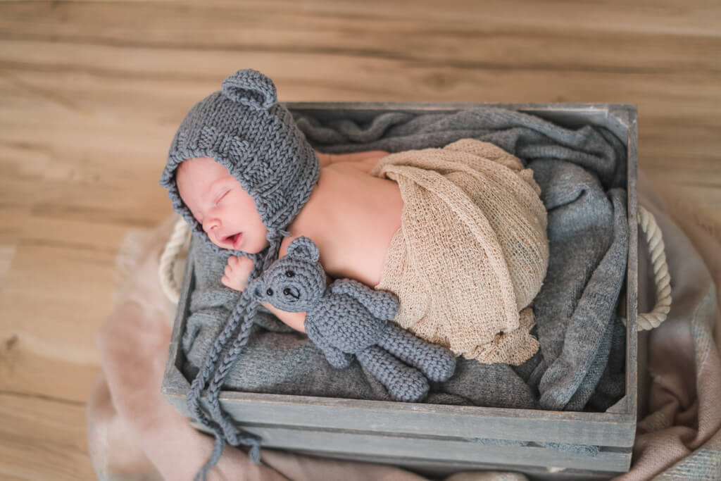 bei der Babyfotografie in Frankfurt liegt in einer grauen Kiste während des Neugeborenenshootings mit einer Bärchenmütze auf.