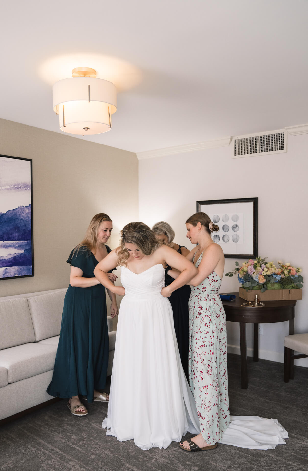 Trauzeuginnen helfen der Braut in ihr weißes Kleid hinein.