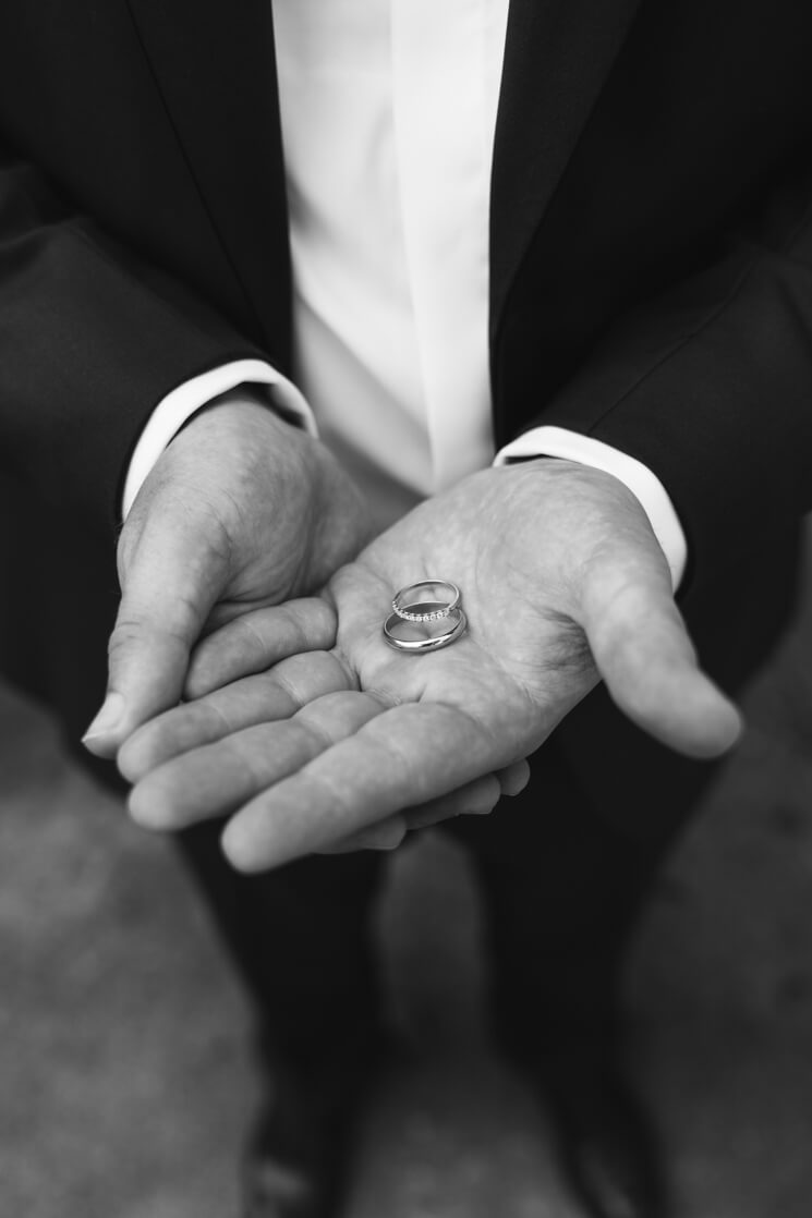 Bräutigam hält beide Eheringe in der flachen Hand.