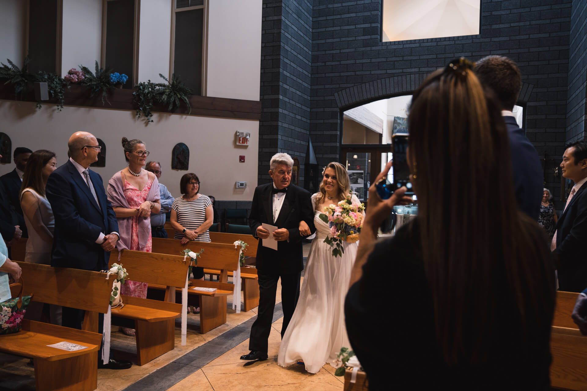 Braut läuft eingehakt in der Hand ihres Vaters zum Altar in einer Kirche in New Jersey.