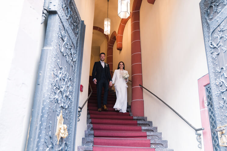 Brautpaar verlässt das Standesamt Frankfurt Römer, über eine alte Treppe mit rotem Teppich.